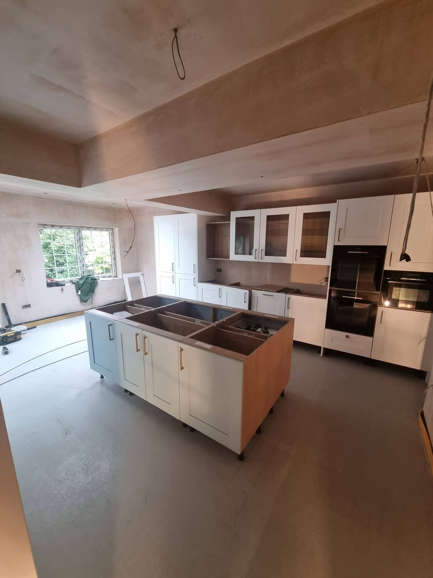 White kitchen cabinets and island during fitting beneath newly plastered ceilings