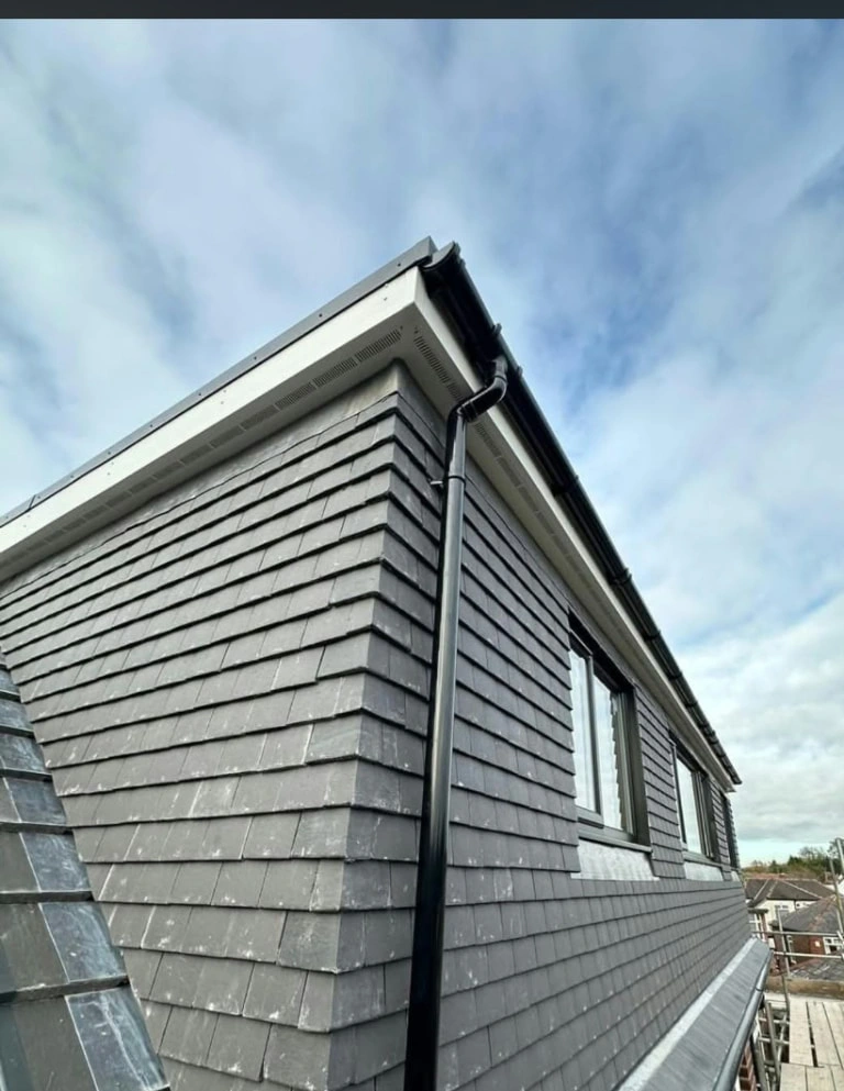 Side view of the Prestwich loft conversion showing dark cladding, windows and guttering beside scaffolding