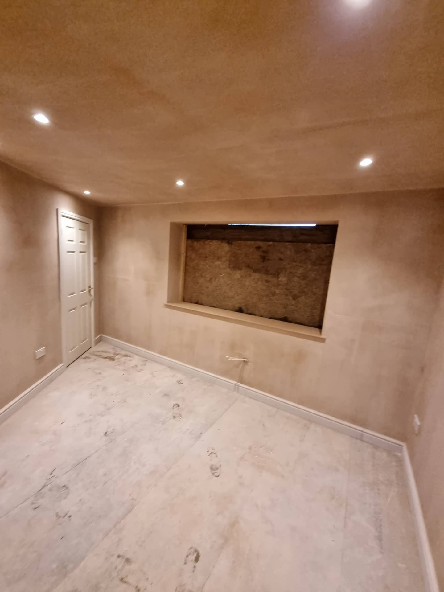 Plastered conversion room with recessed lights, a boarded window opening and unfinished floor