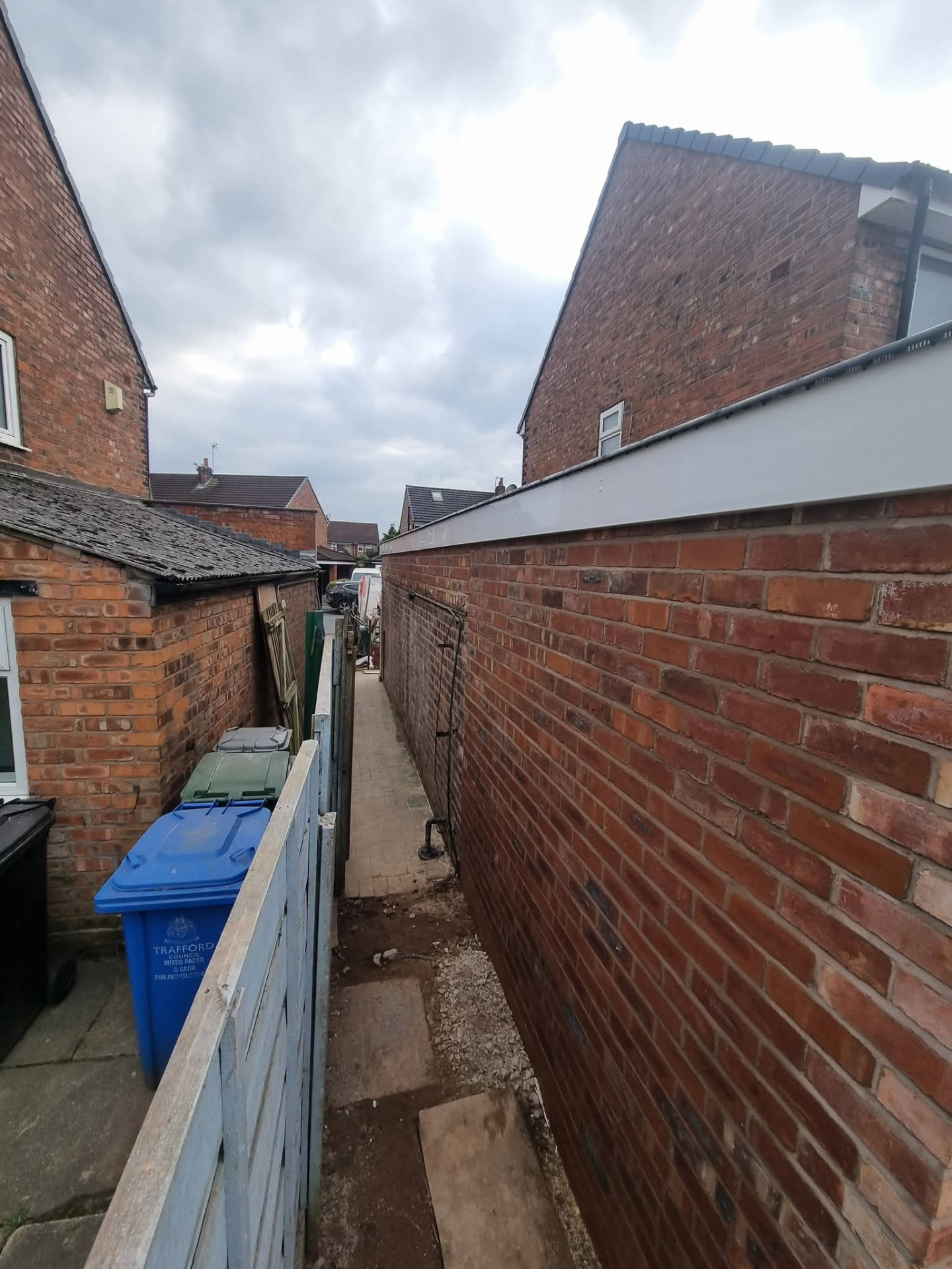 Side extension brick wall with white fascia and black gutter beside a narrow passage