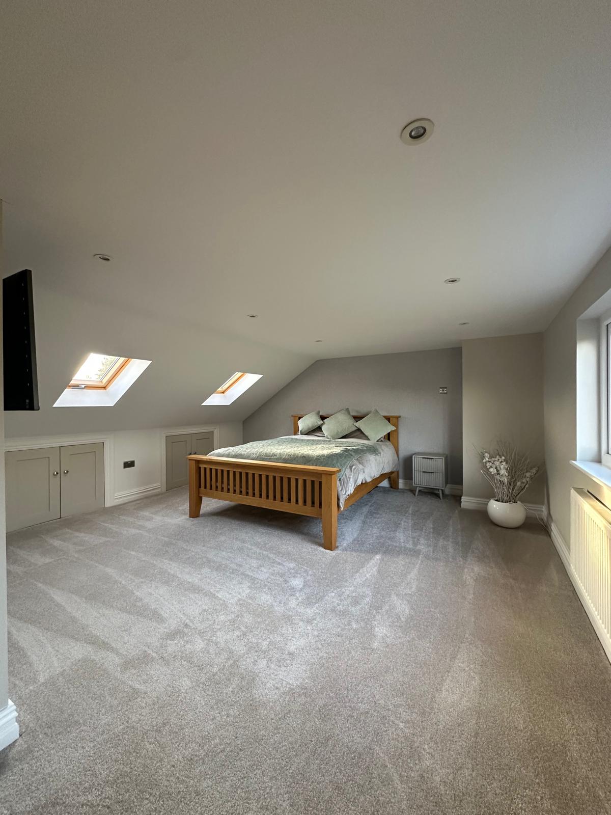 Finished loft bedroom in Romiley with rooflights, eaves cupboards and a wooden bed