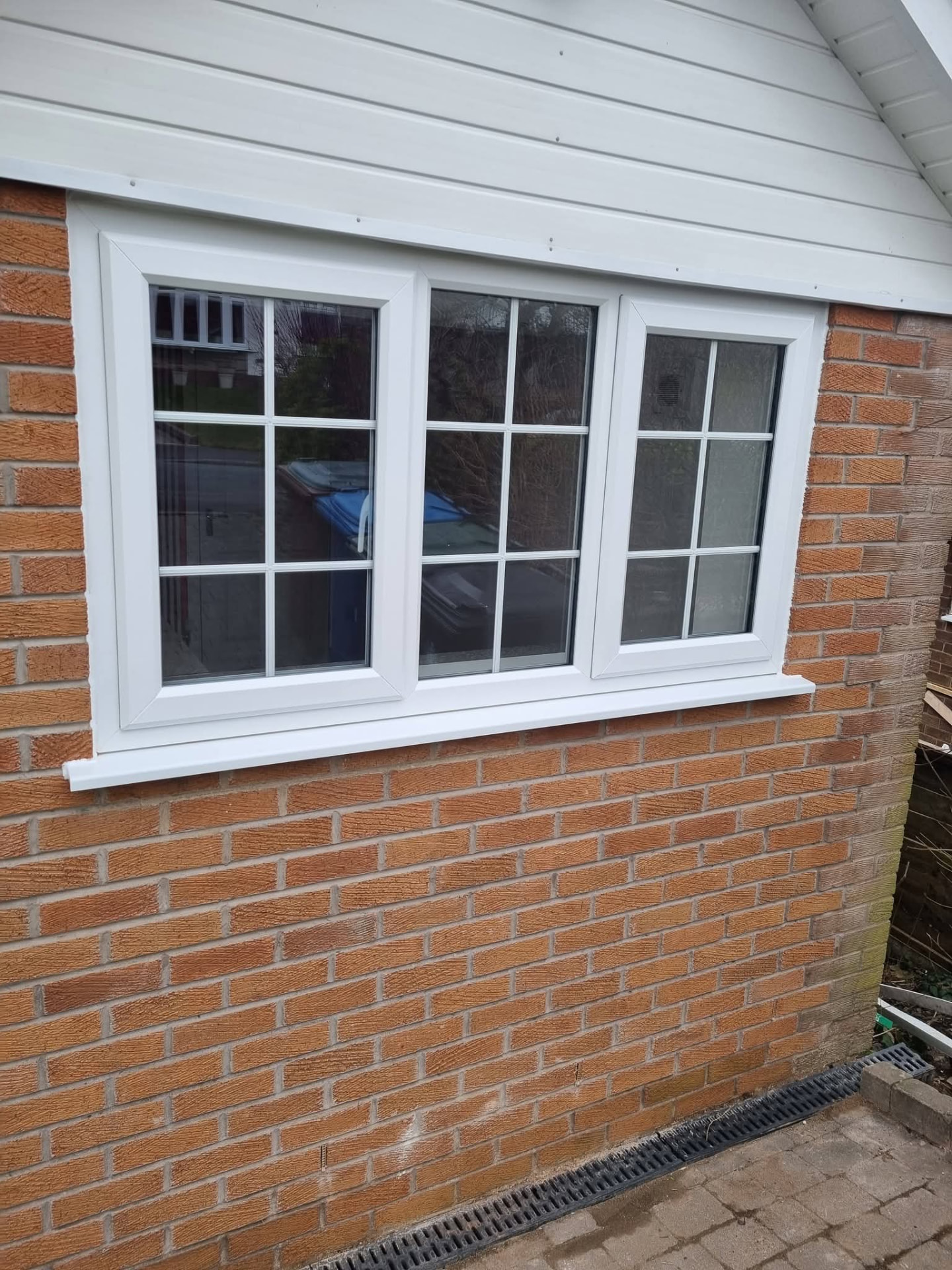White-framed window with glazing bars in a red-brick wall beneath white cladding