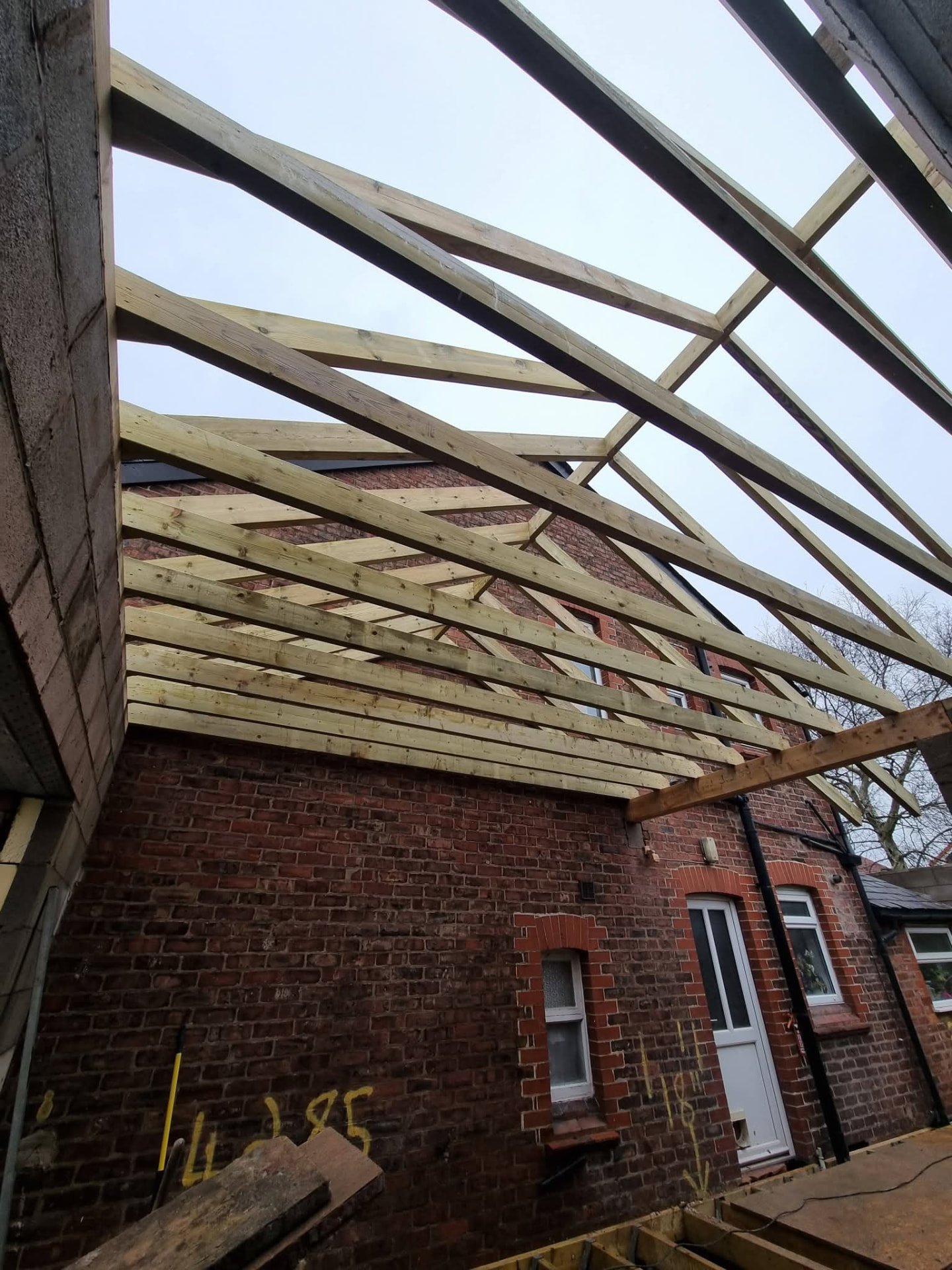 Pitched timber roof framing viewed from below beside the brick house