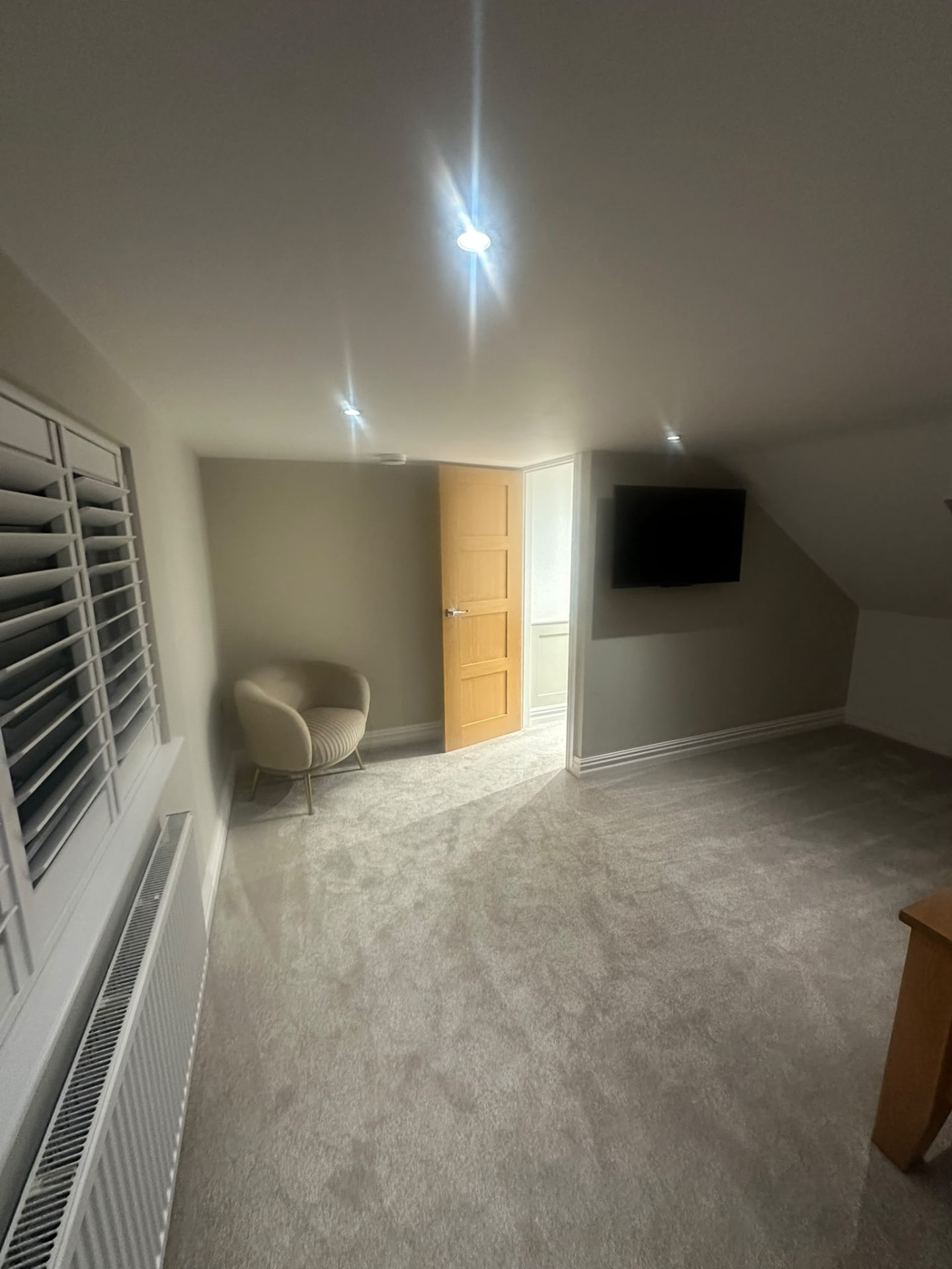 Finished loft bedroom with timber door, wall-mounted television and sloping ceiling