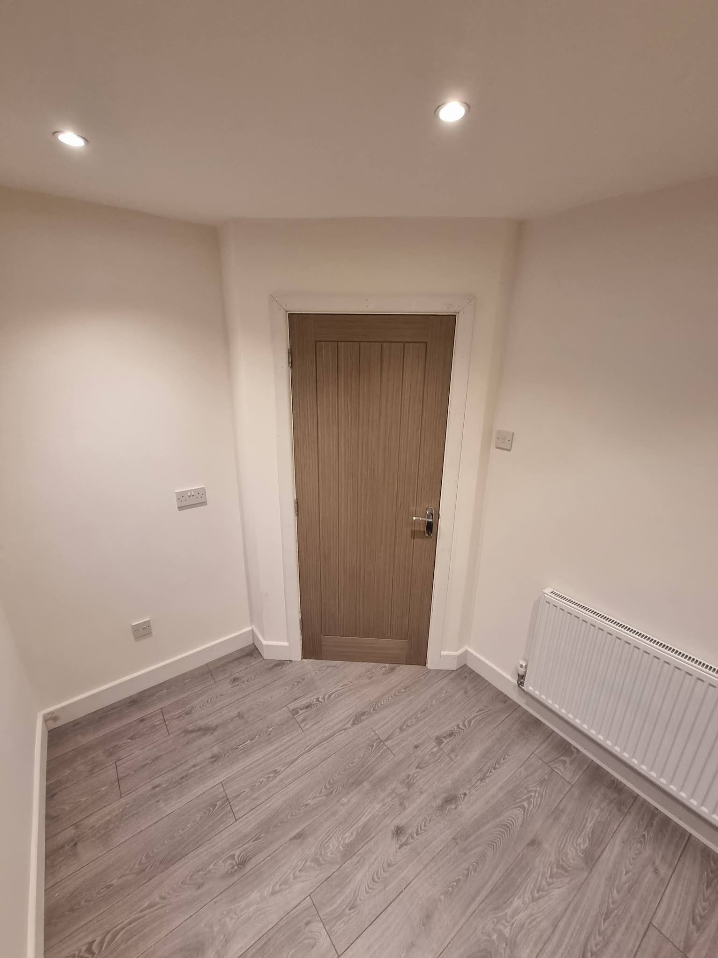 Finished room with timber door, radiator and recessed ceiling lights