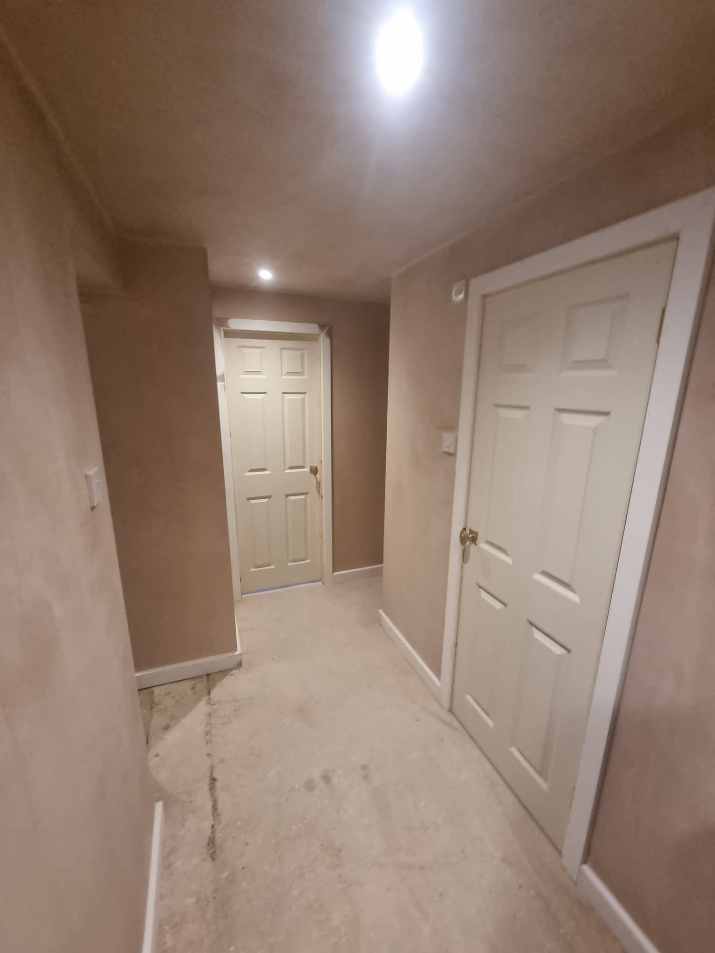 Newly plastered hallway with two white doors, recessed ceiling lights and unfinished floor