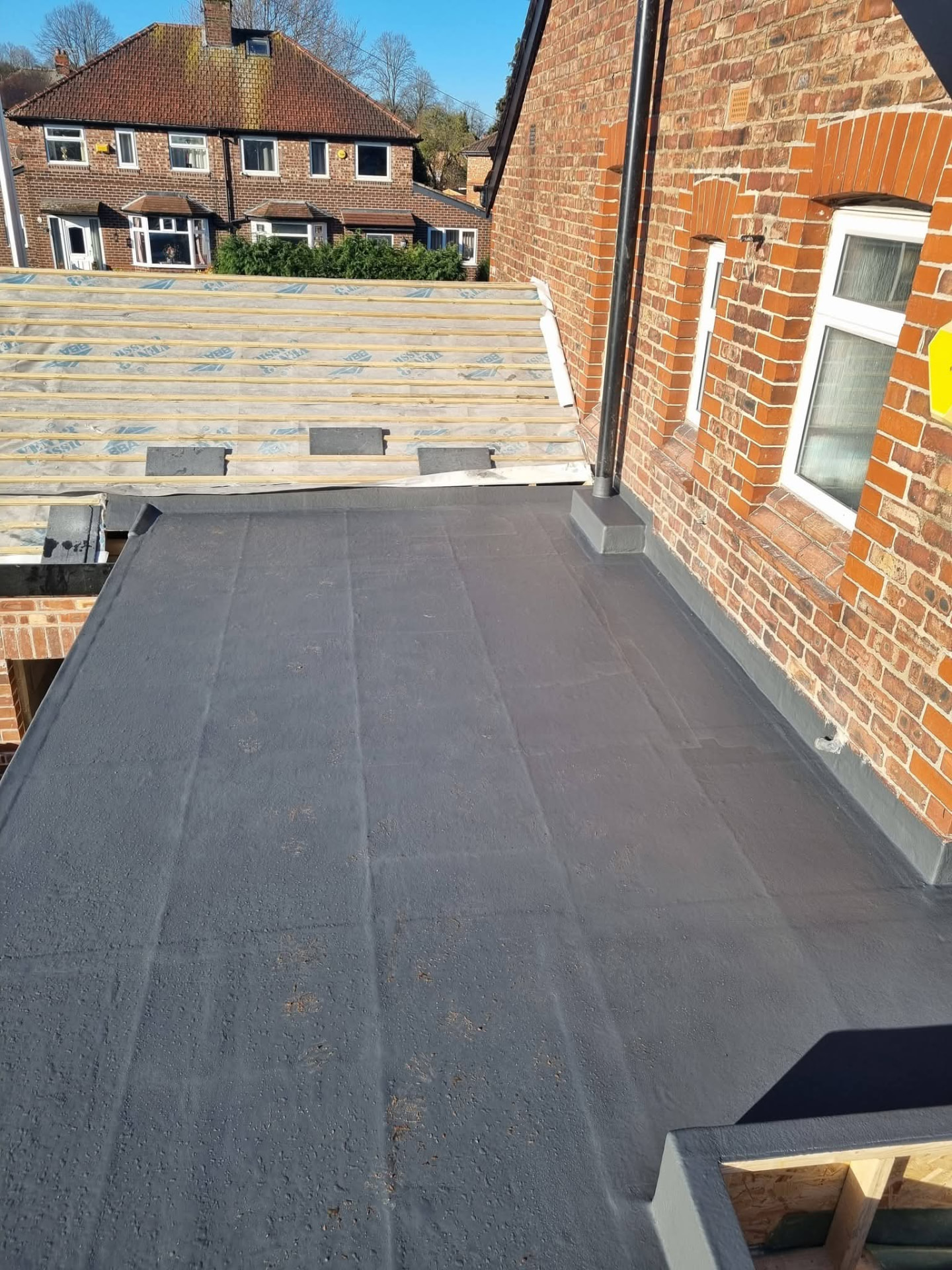 Flat roof covering adjoining timber roof battens beside the brick house