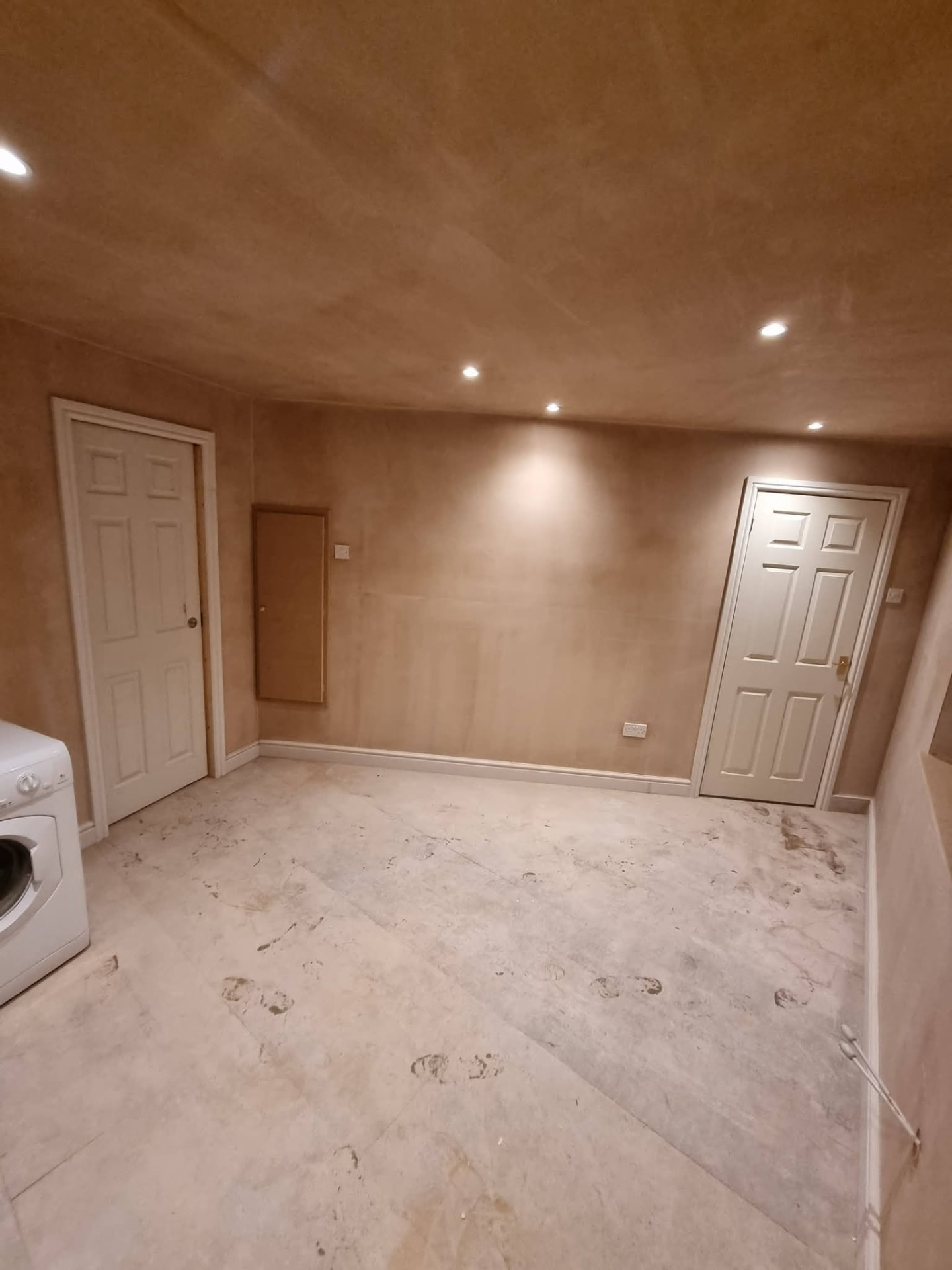 Newly plastered conversion room with two white doors, recessed lights and unfinished flooring