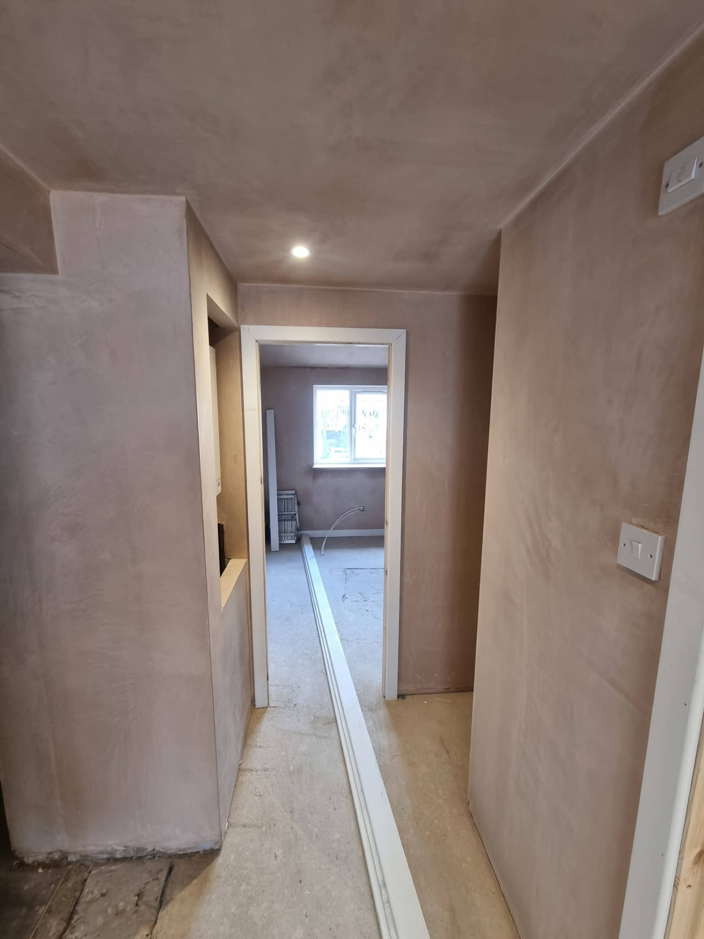 Plastered hallway leading to a room with a white-framed window during interior finishing