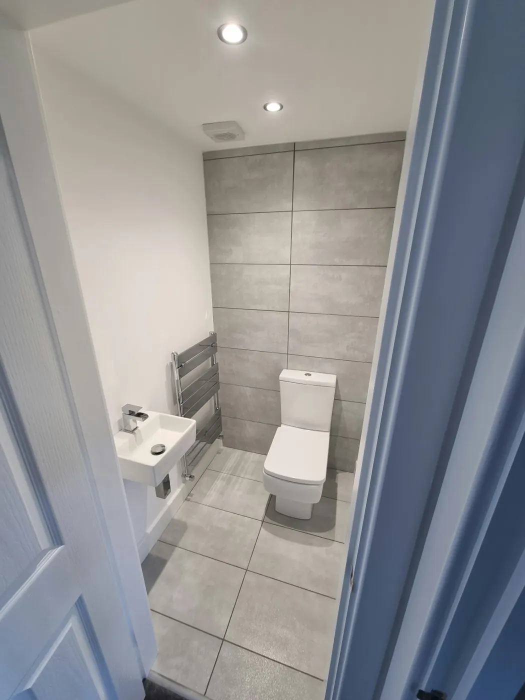 New downstairs WC in Marple with grey wall and floor tiles, compact basin and chrome towel radiator