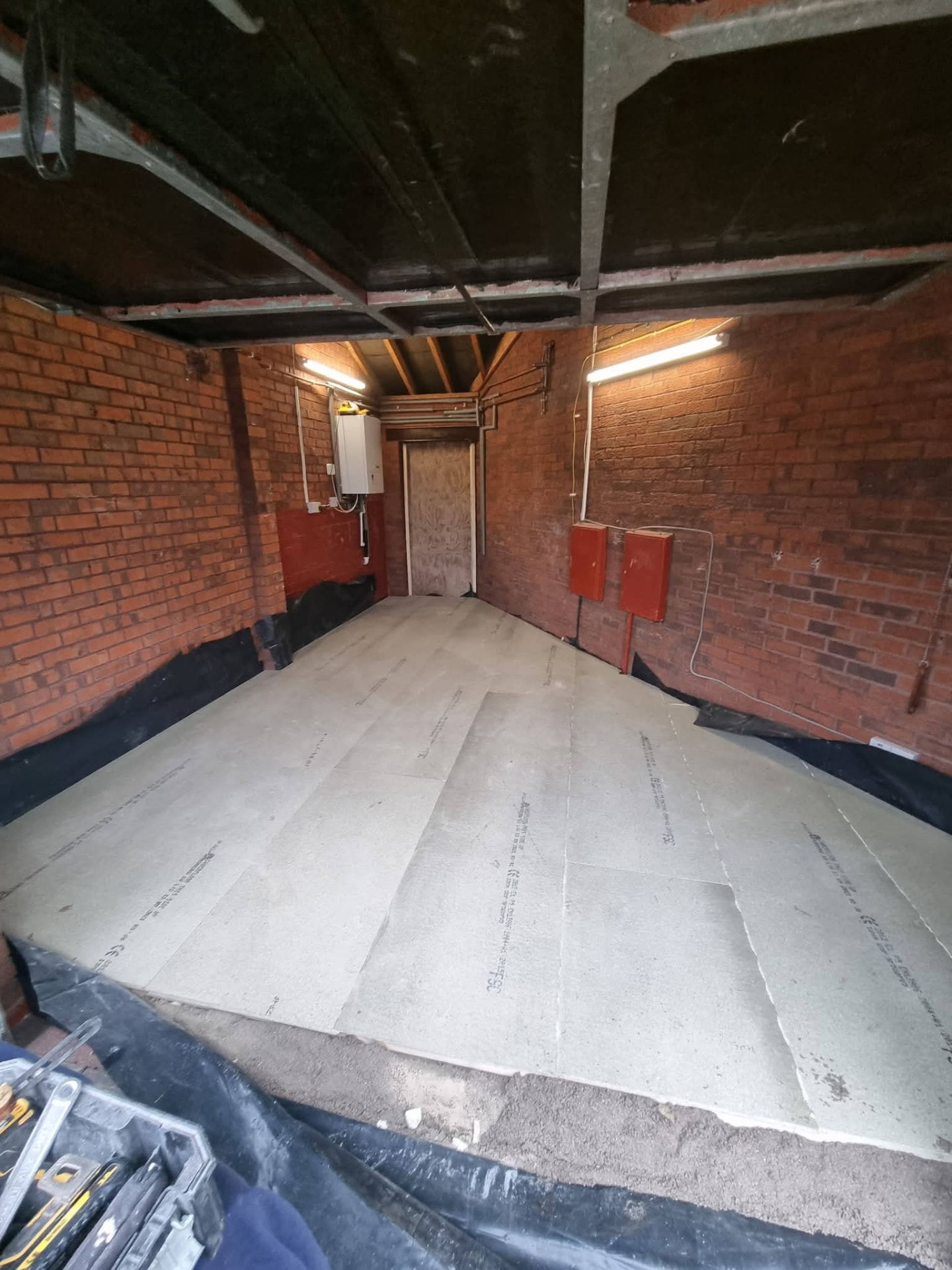 Garage interior with exposed brick walls and insulation boards laid across the floor