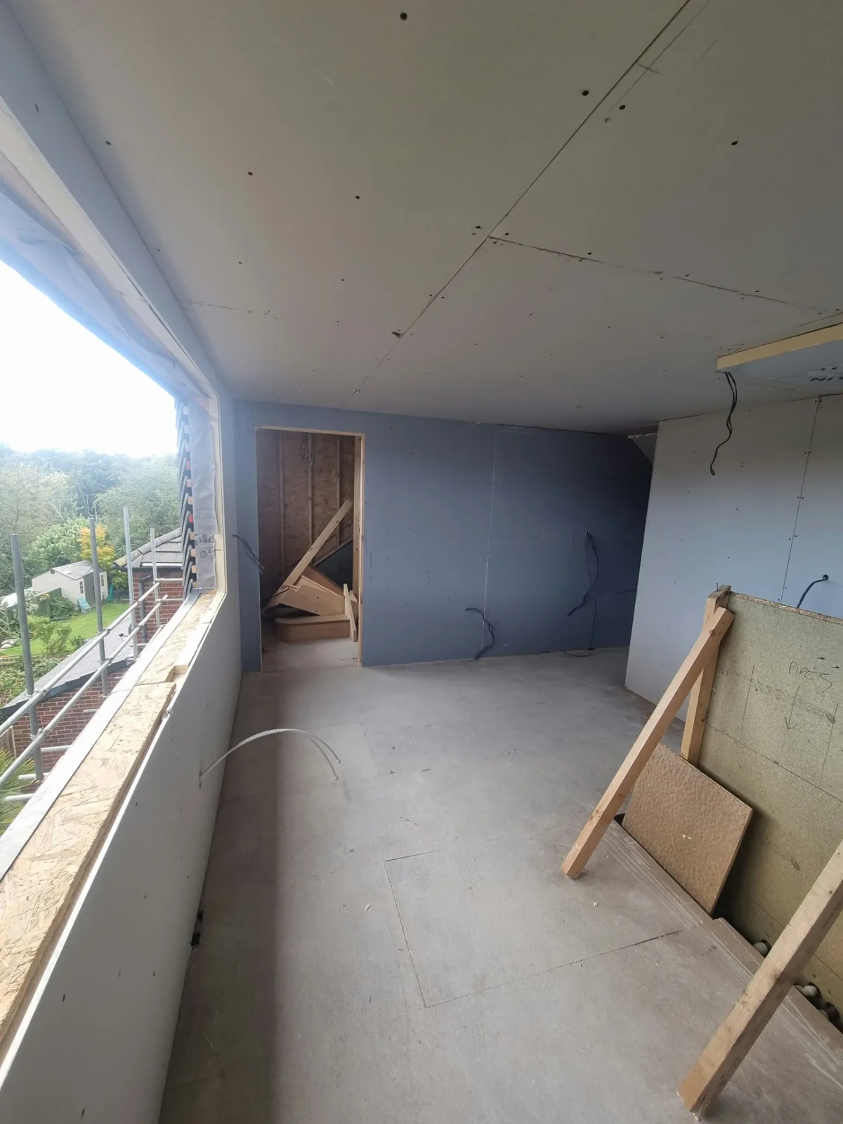 Plasterboarded loft room at the Prestwich project before finishing, with a wide window opening