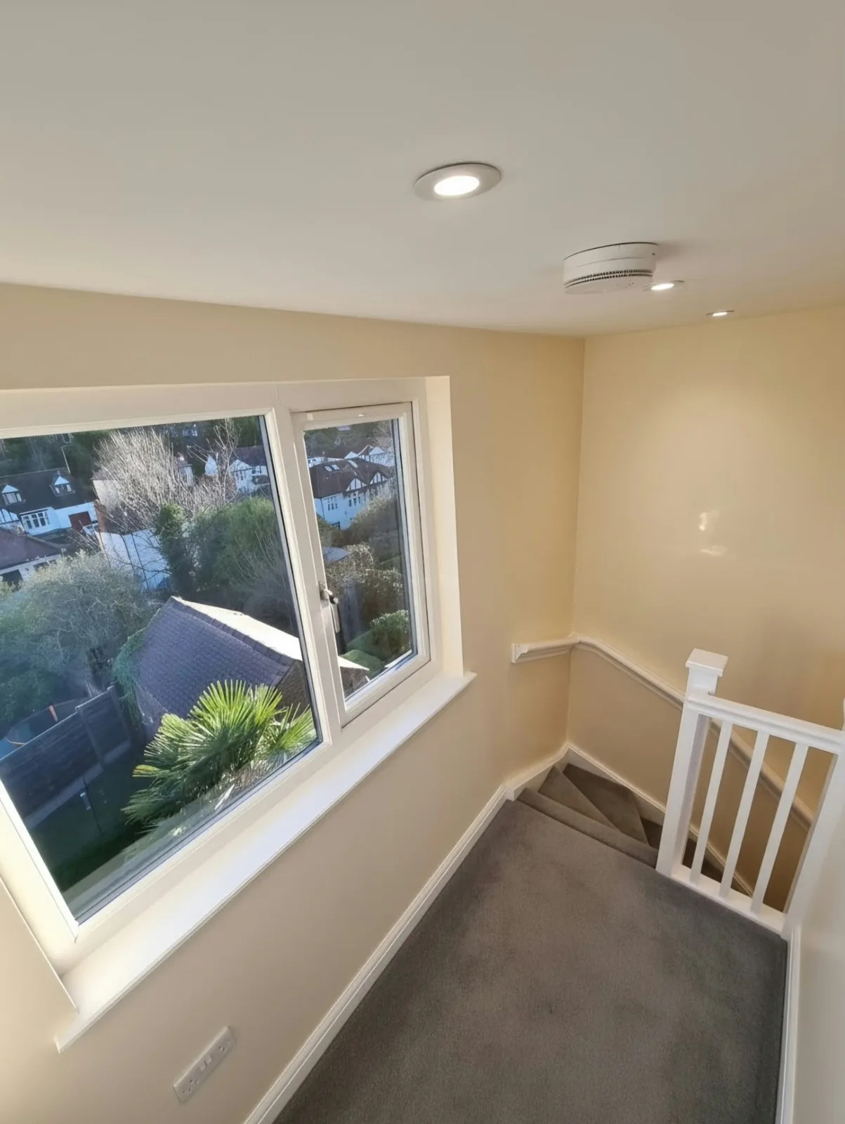 Finished carpeted loft landing in Prestwich with a wide window, white balustrade, handrail and recessed ceiling lights