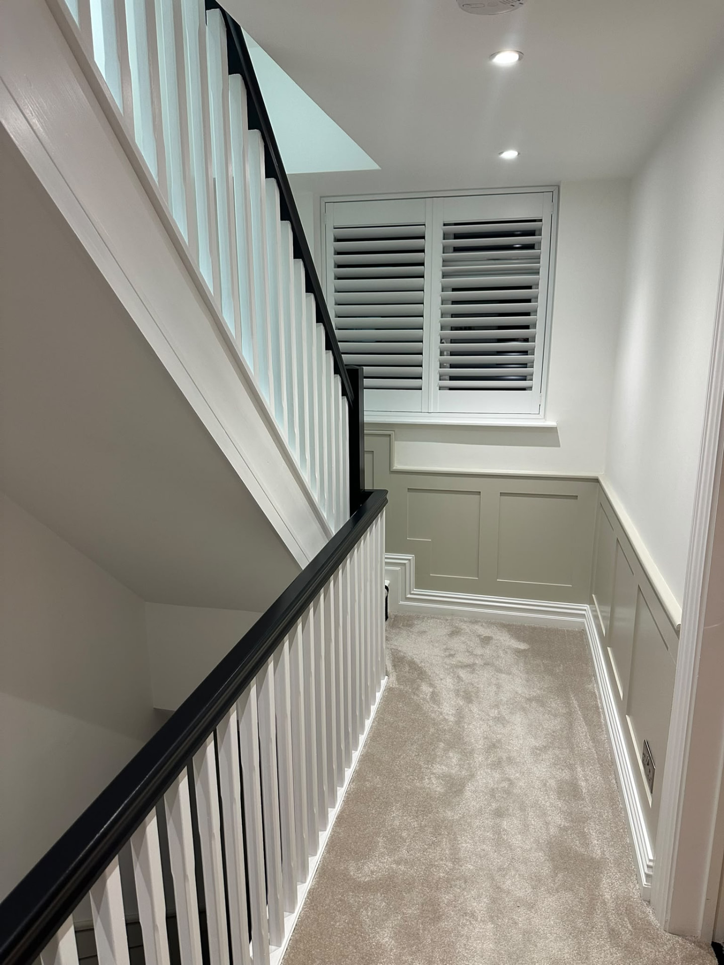Finished carpeted landing with white balustrades, dark handrail and panelled walls