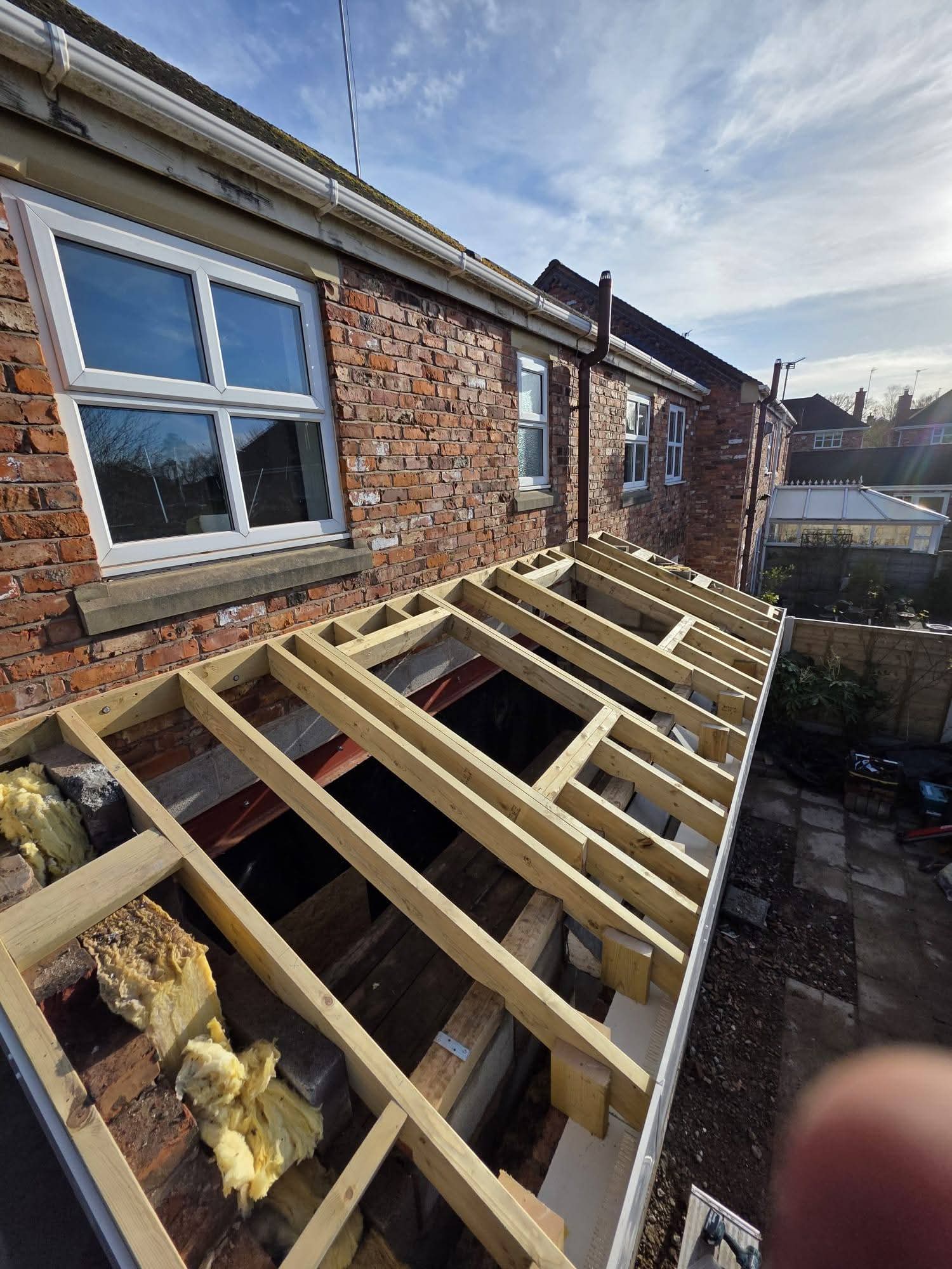 Lean-to timber roof framing with roof window openings beside the brick house