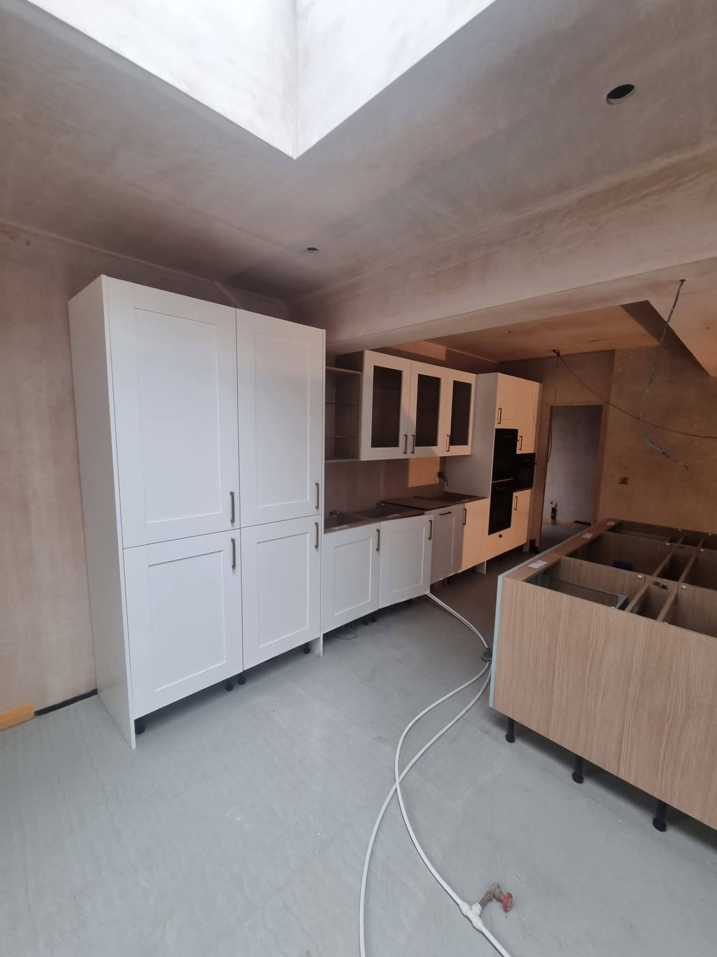 White kitchen cabinetry during fitting beneath a rooflight opening