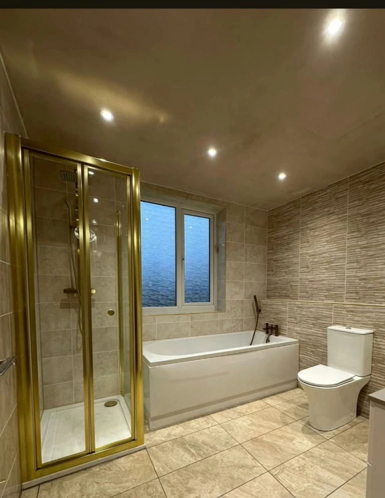Finished bathroom at the Prestwich project with gold-framed shower, bath, toilet and tiled floor