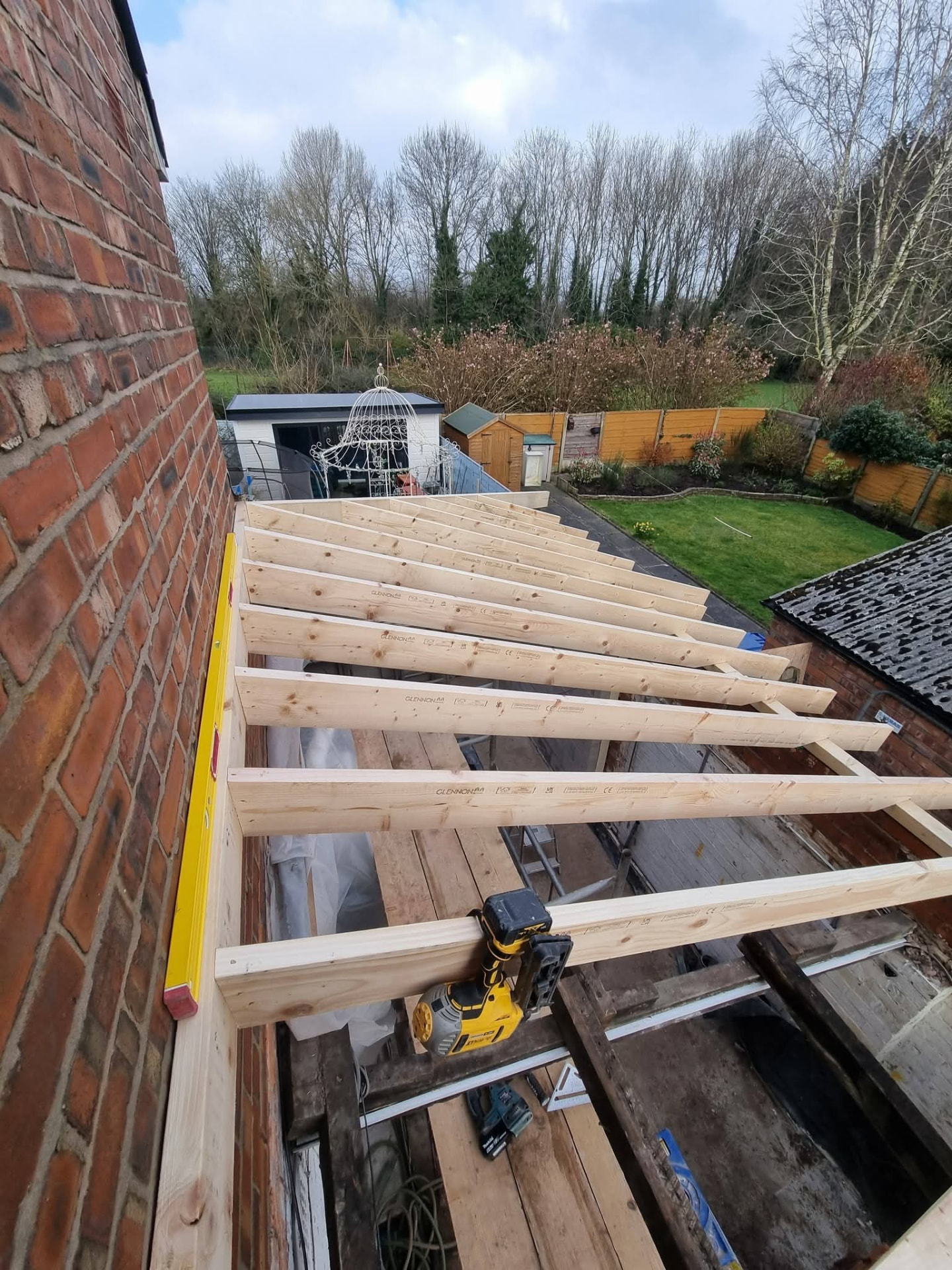 Extension roof rafters viewed from above beside the existing brick house
