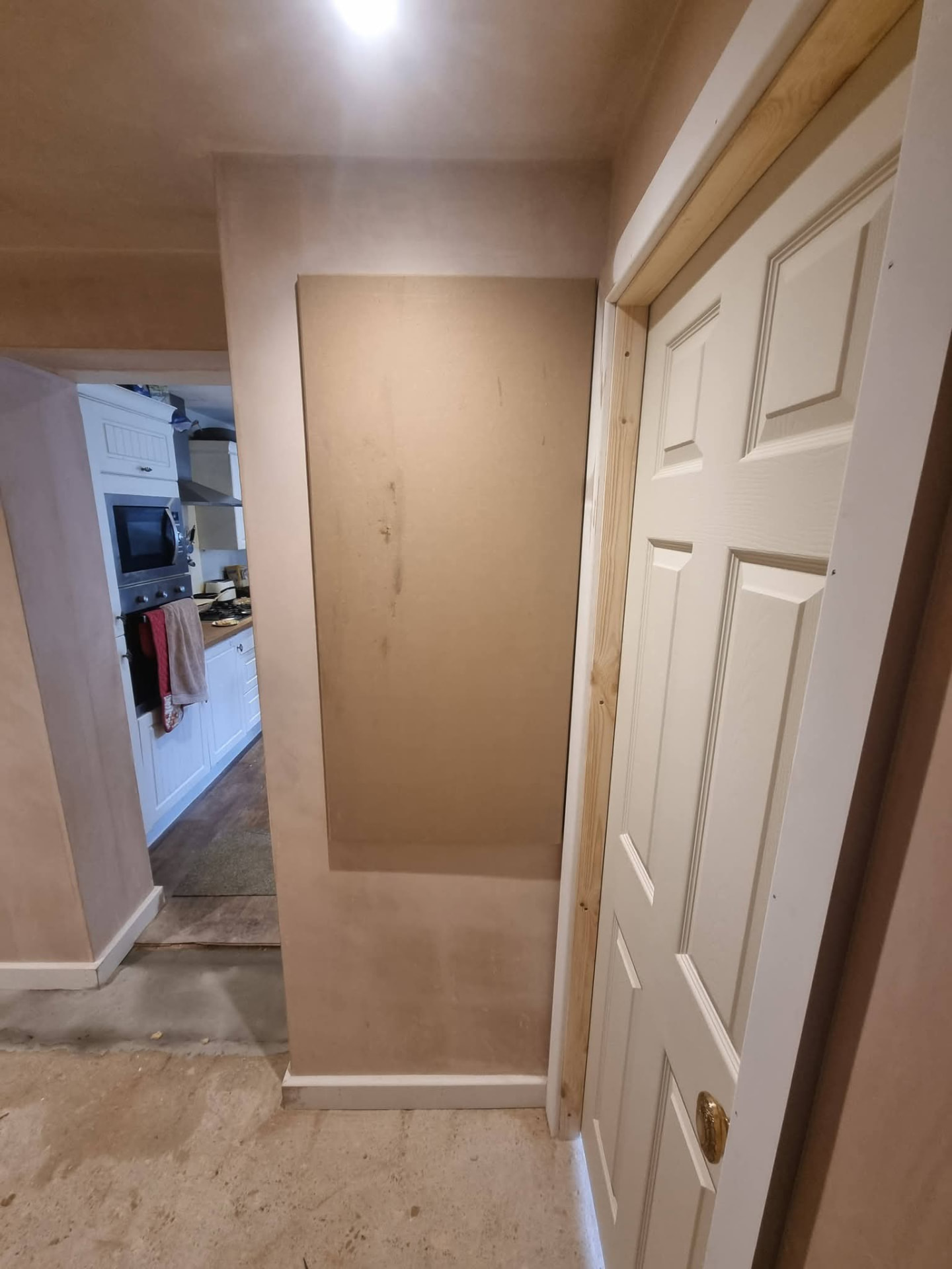 Newly plastered hallway with white door and an opening towards the existing kitchen