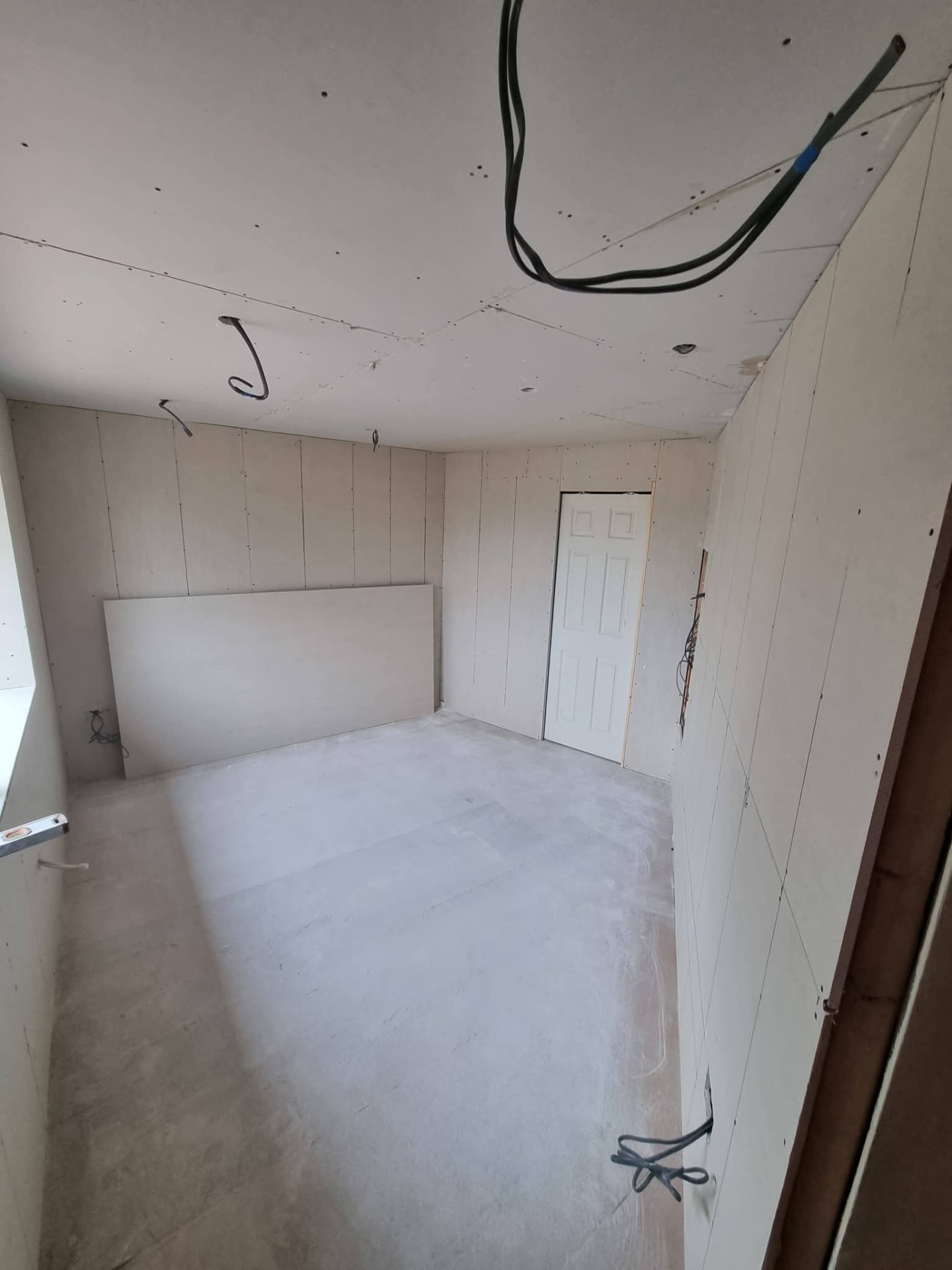 Plasterboard-lined conversion room with white door and hanging electrical cables