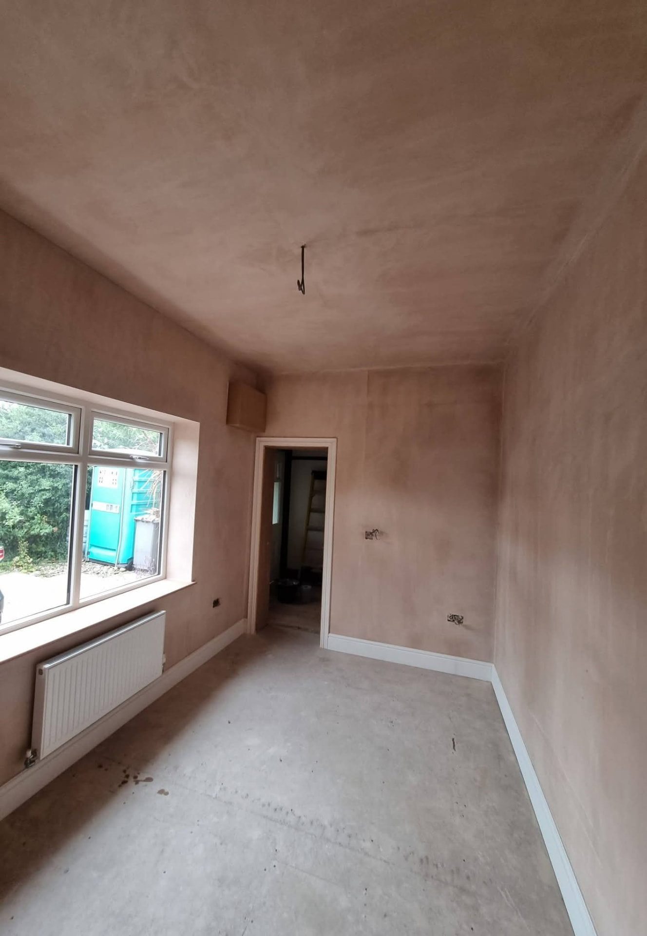 Newly plastered room with window, radiator and unfinished floor