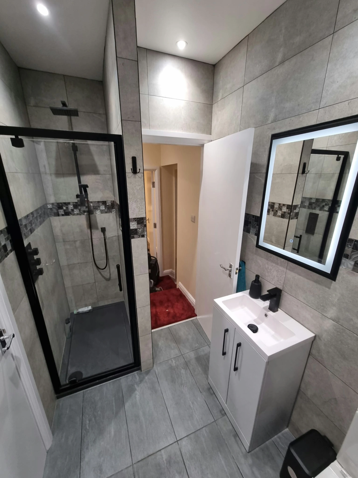 Finished tiled shower room at the Prestwich project with black-framed shower enclosure, vanity basin and illuminated mirror