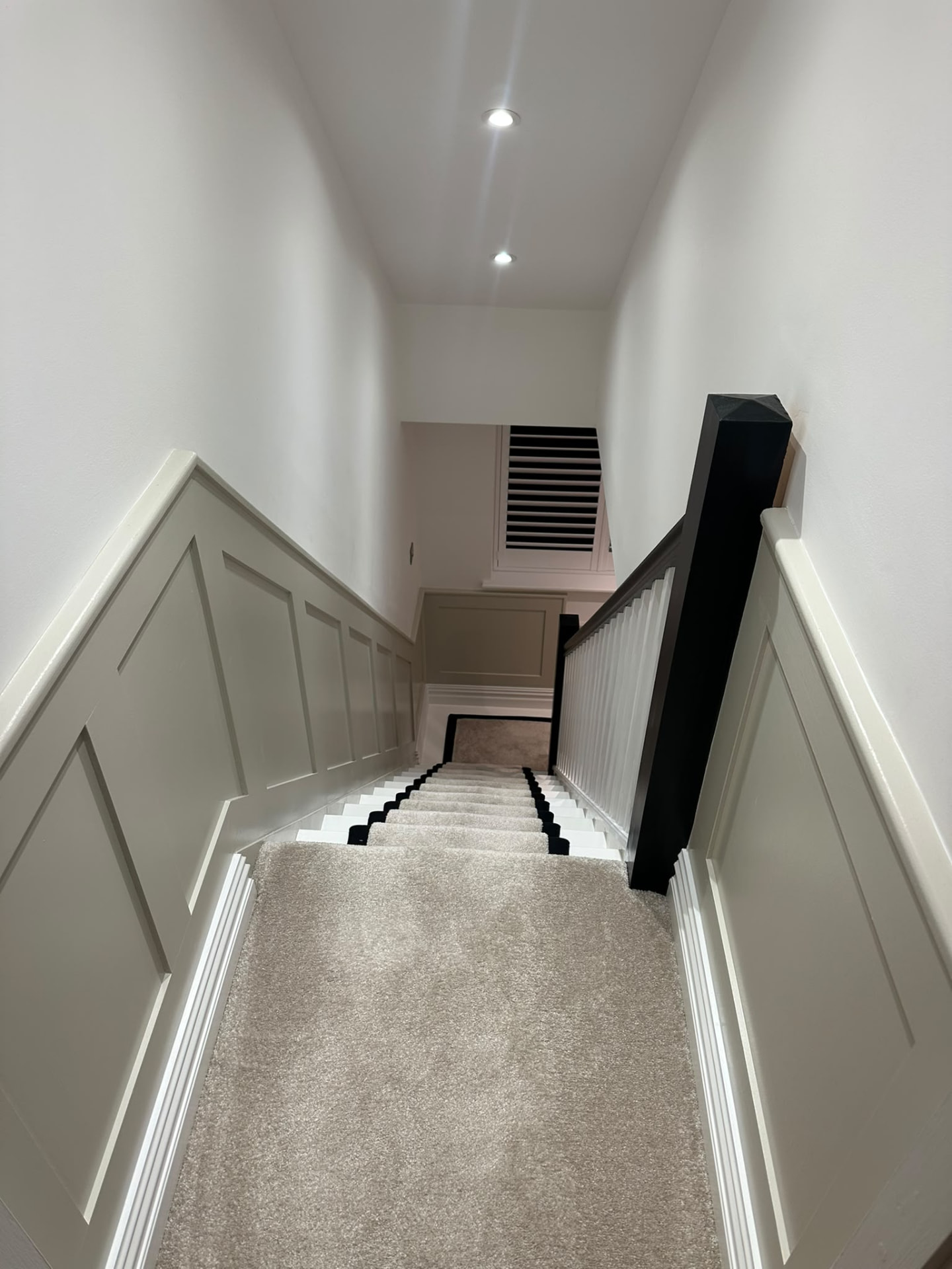 Finished loft staircase with carpeted treads, dark handrail and wall panelling